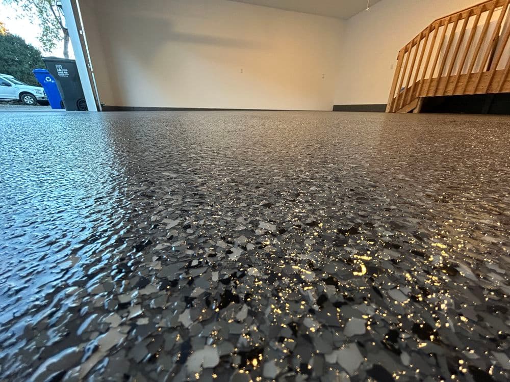 Glossy epoxy garage floor with decorative flakes and wooden stairs in background.