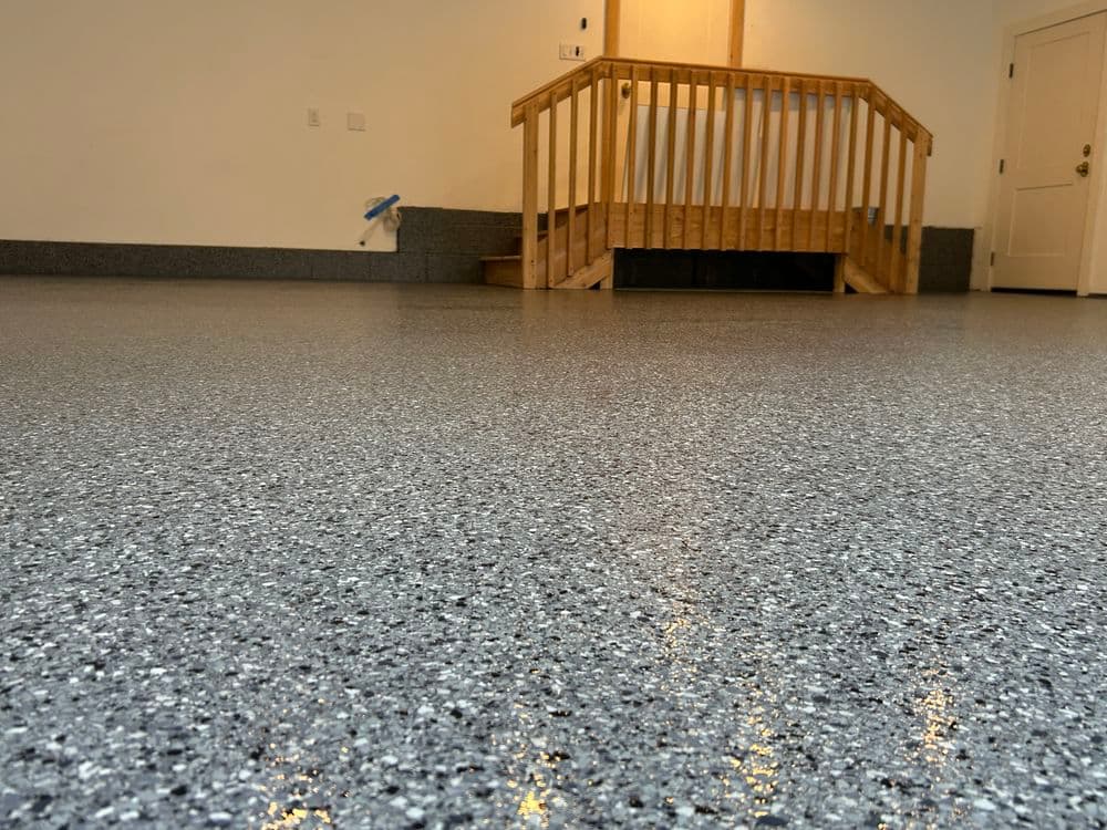 Epoxy-coated garage floor with gray and black speckles, featuring wooden steps in the background.