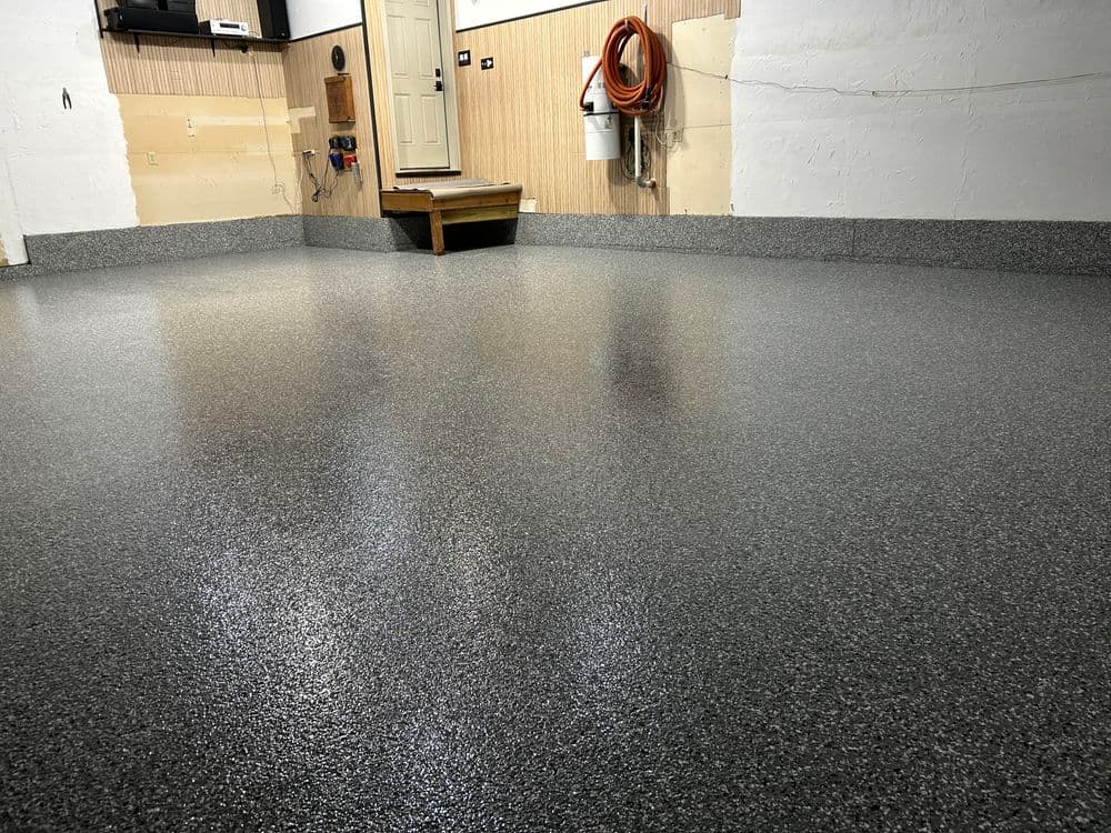 Glossy black and gray epoxy garage floor with wooden step and door in background.