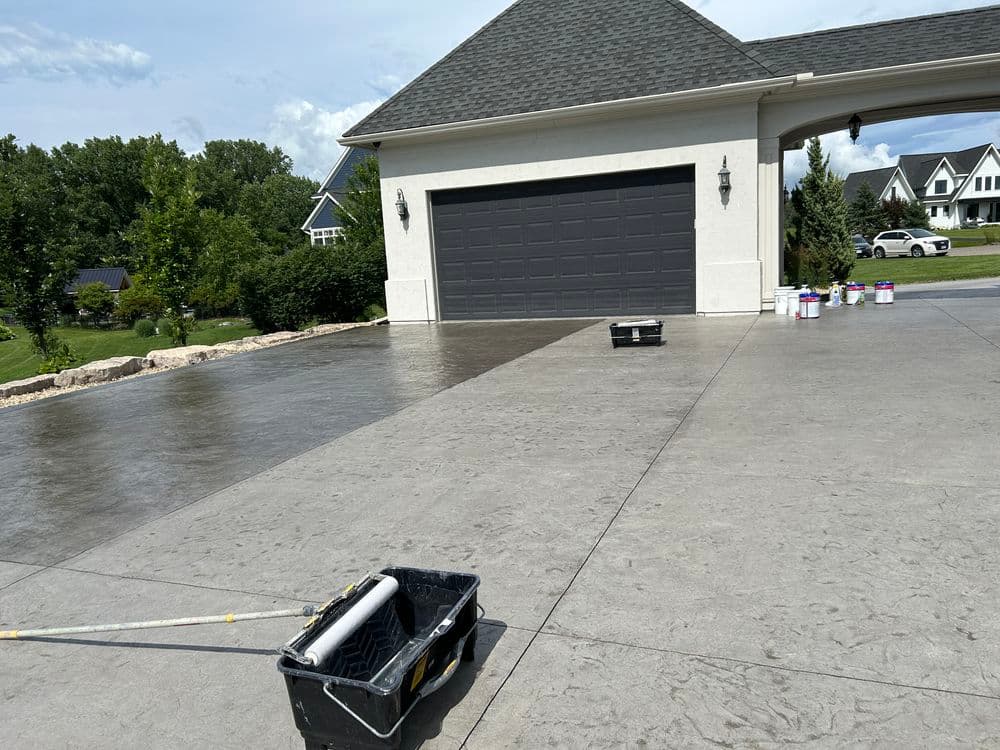Freshly painted concrete driveway and garage with paint supplies visible in sunny residential setting.