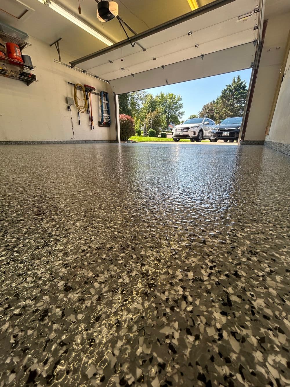 Garage interior with a shiny, speckled epoxy floor and daylight entering through the open door.