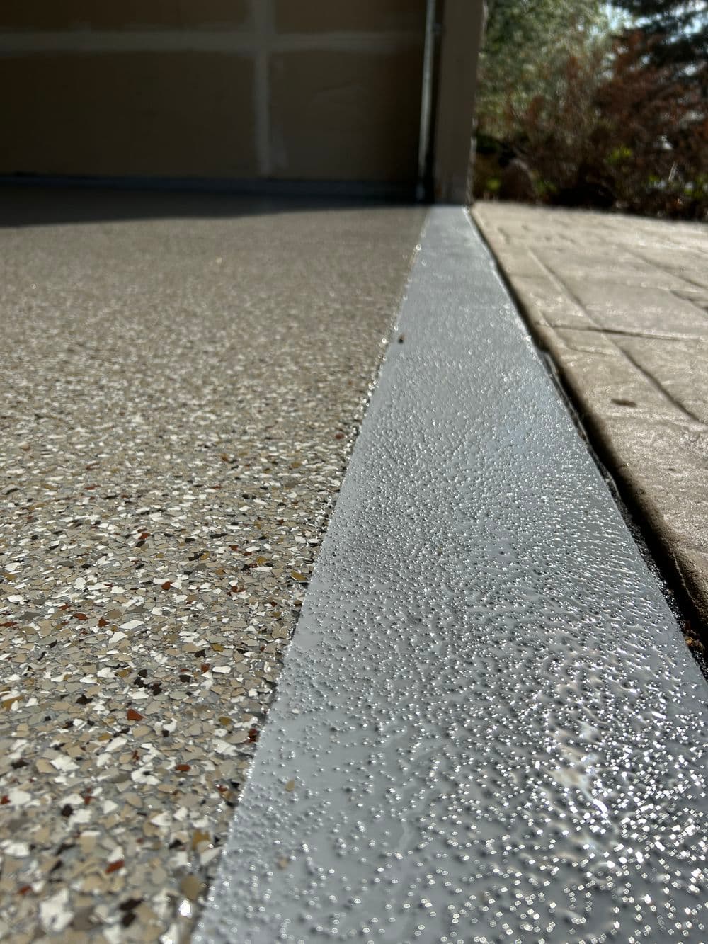 Close-up of a textured garage floor with a gray edge trim and water droplets.