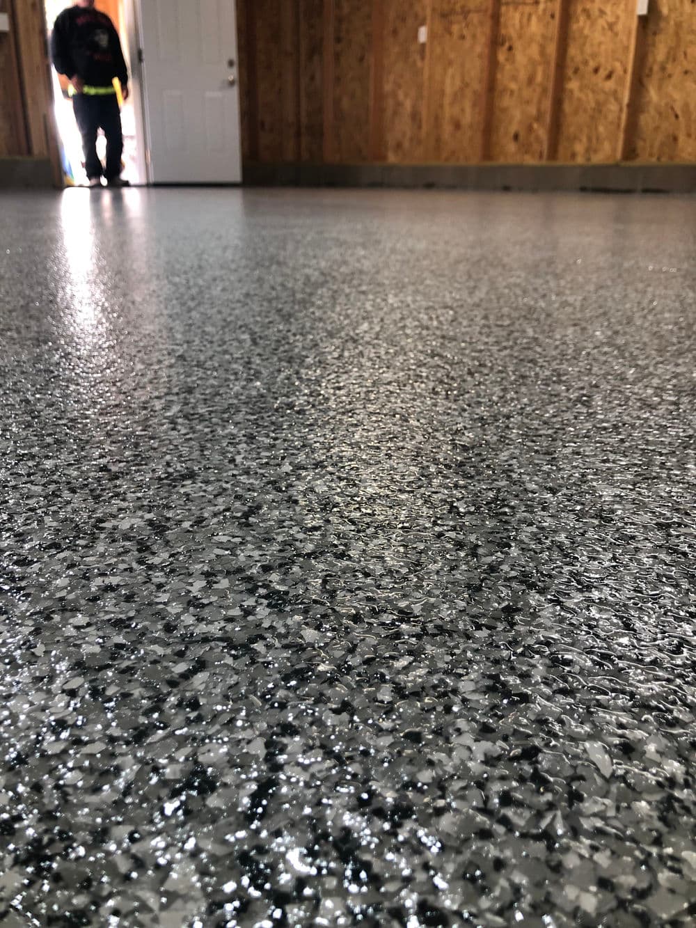 Close-up of a shiny, textured gray epoxy garage floor with a person in doorway.